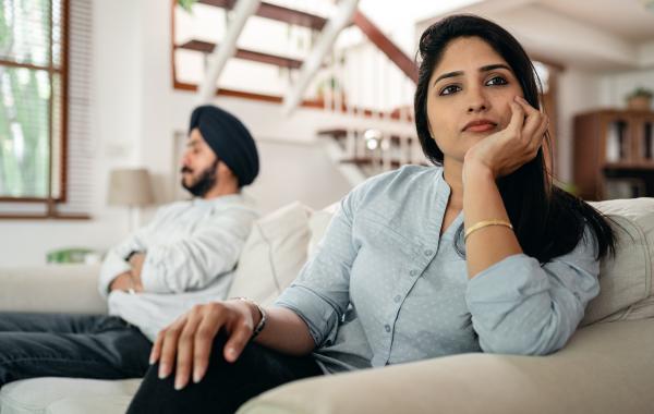 A man and woman sat on a sofa, turned away from each other