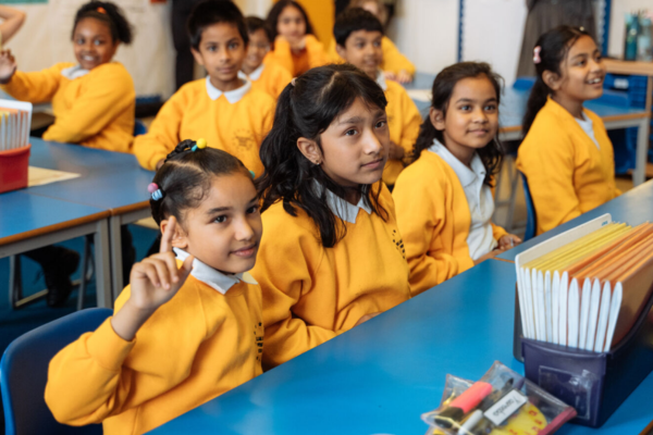 Girls in a classroom, with one raising her hand