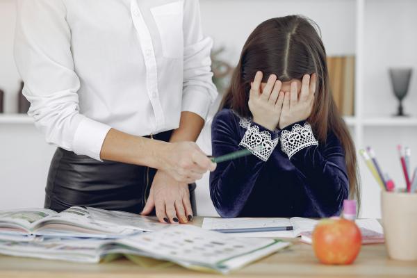 A child covering their face and looking stressed while doing homework